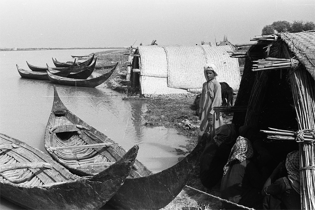 Watched by men sitting in a small mudhif, Bin Thuqub appears to pause as Thesiger makes this photo at the edge of a village that shows a broad waterway as well as the simple efficiency of the tarada. Spending time out on the water, Bin Thuqub recalls, “We considered it as having fun, and having a good time with friends. We considered the marshes as having great value and legacy. We knew that.”